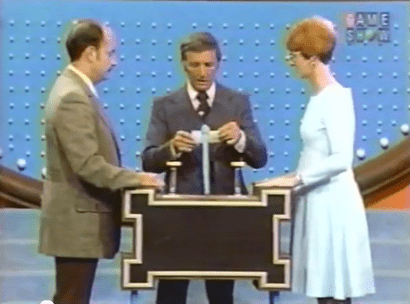 Photo of Richard Dawson at the podium of family feud, asking a question to contestants