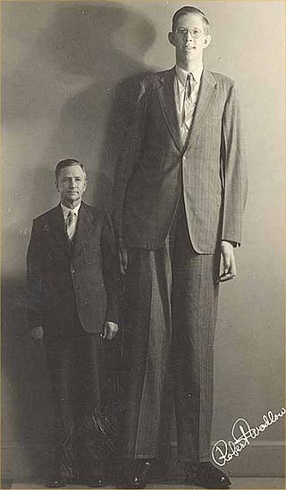 A photo of Robert Wadlow, incredibly tall and smiling, standing in a baggy suit next to his much shorter dad