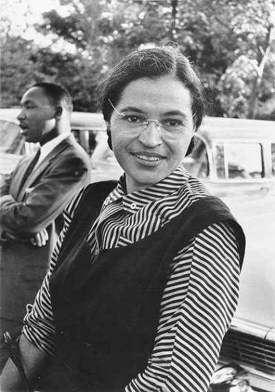Photo of Rosa Parks smiling at a park, with Martin Luther King in the background