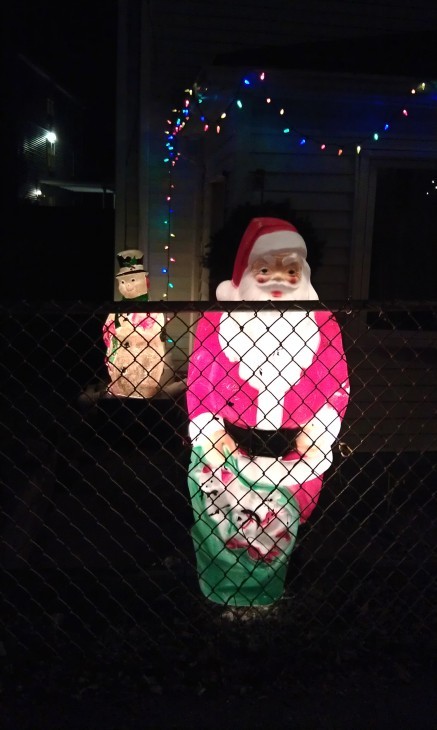 Photo of Santa Claus in a front yard behind a wire link fence