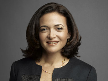 Sheryl Sandberg photo with short brown hair and a handsome charcoal open-collar suit, smiling