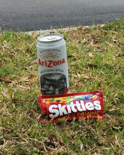 A photo of Skittles and iced tea, set in the grass outside a 7-11 store