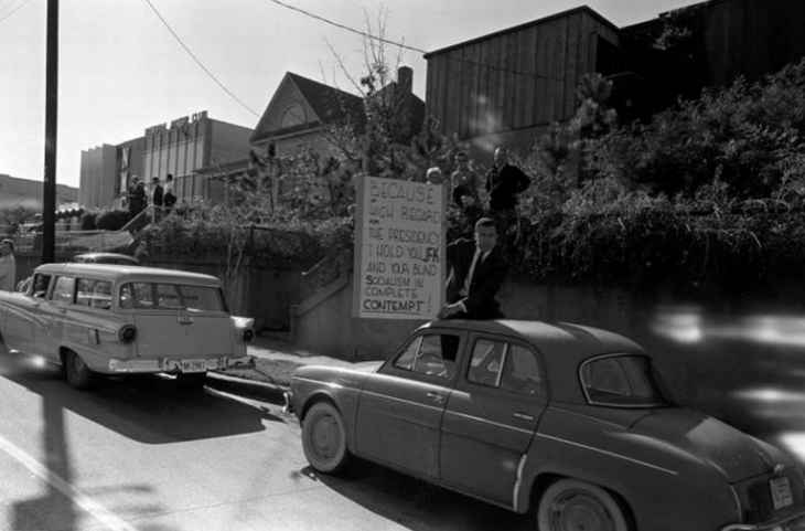 Photo of a protester holding a sign accusing JFK of 