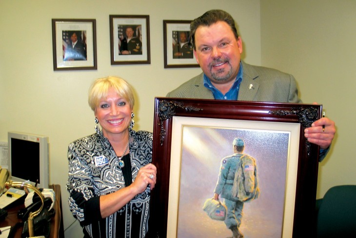 Photo of Thomas Kinkade posing with a painting of a soldier and a woman who runs the USO