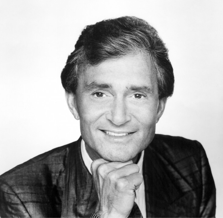 A close-up photo of Vidal Sassoon, chin on his hand, smiling for the camera