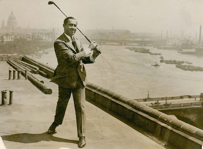Walter Hagen stands on a rooftop, dressed in a full business suit, swinging a golf club