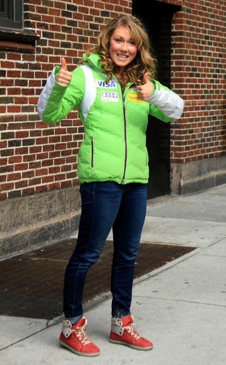 Mikaela Shiffrin photo in a green jacket and red tennis shoes, on the sidewalk in New York giving a thumbs-up