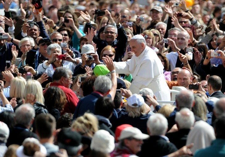 A photo of Pope Francis, smiling, surrounded by crowds and cameras in St. Peter's Square