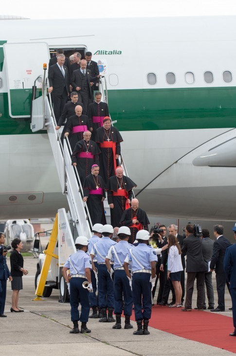 Photo of many black-and-red robed cardinals exiting a plane on steps