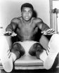 Muhammad Ali, young and fit with rippling muscles, leans forward to touch his toes on a leather training table (or chair?) of some kind