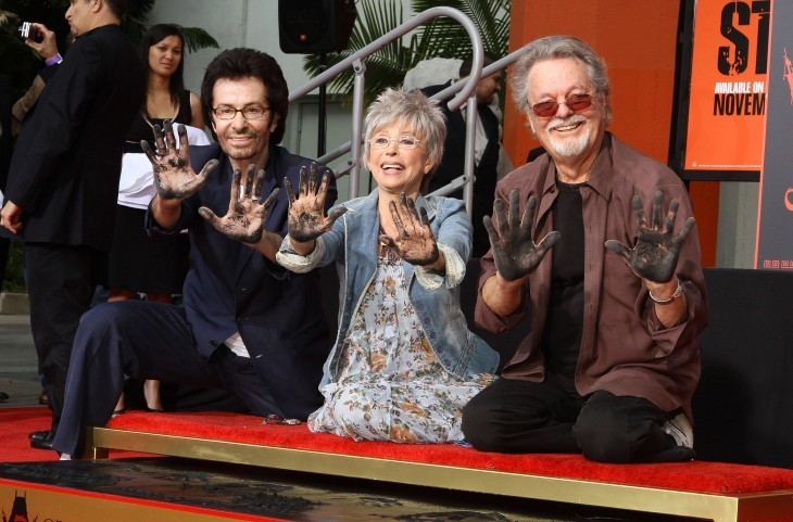 Three actors smile as they show hands covered with cement