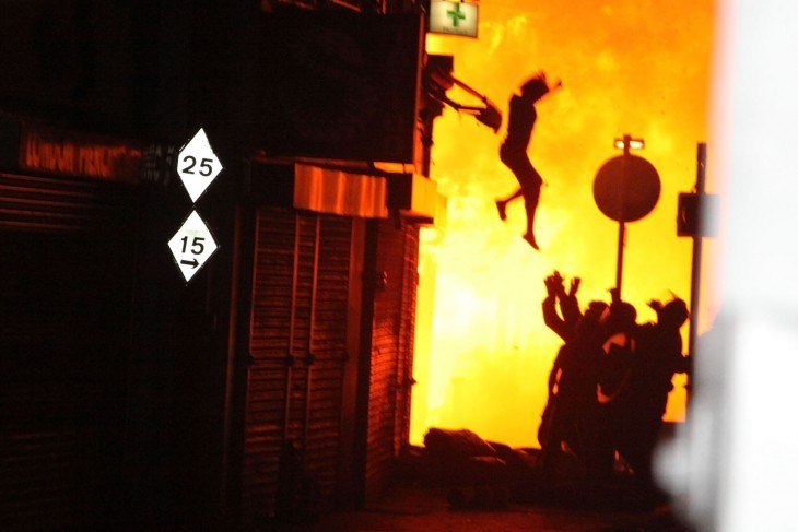 A woman jumps from the second floor of a burning building as firefighters wait below, arms outstretched, to catch her