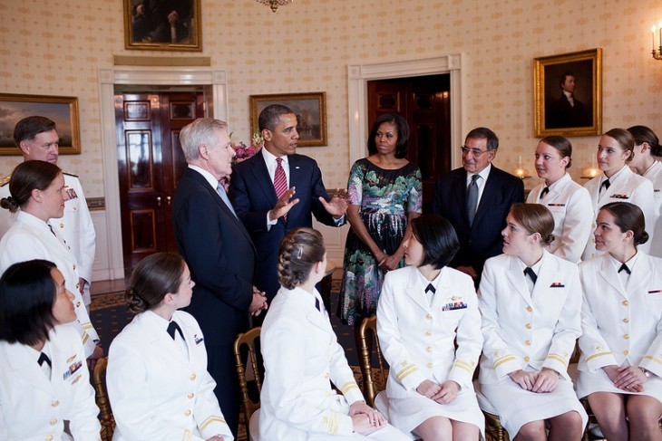 Photo of women sailors in white suits, seated, turning to listen to President Obama and the First Lady