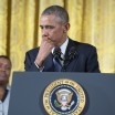 Photo of Barack Obama standing at podium with the presidential seal, pausing with hand to mouth and looking a little bit teary