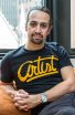 Lin-Manuel Miranda photo portrait, with Miranda wearing a goatee and a blue t-shirt reading ARTIST in big cursive script