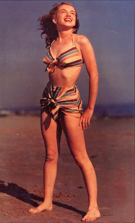 Marilyn Monroe smiles in the sun on a sandy beach, smiling at the sky