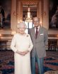 Queen Elizabeth II and Prince Philip stand in a fancy gilded room in Buckingham Palace, she in a knitted dress and he in a sport coat