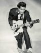 Chuck Berry duckwalks toward the camera, guitar at the ready. He's wearing a nice pair of tan Oxford shoes