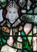 A solemn-looking saint, wearing a miter with a cross and green robes, in a stained-glass window