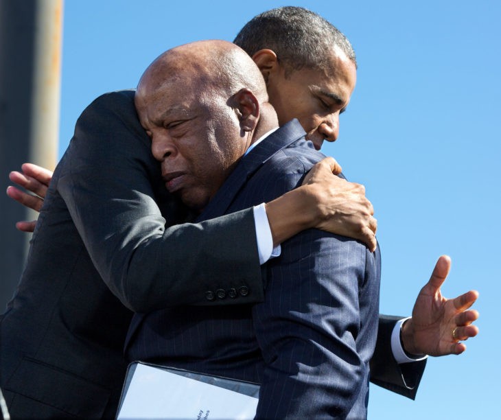 Barack Obama (young and tall) shares an emotional hug with John Lewis (older and shorter) as they stand at the end of a bridge with blue sky above them