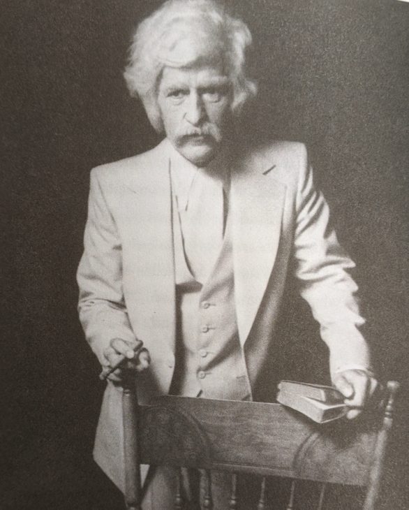 Alex Trebek dressed as Mark Twain in a white suit and holding a cigar. He has bushy gray hair and a bushy Twain-style moustache, and darned if he doesn't actually look a good deal like Mark Twain.