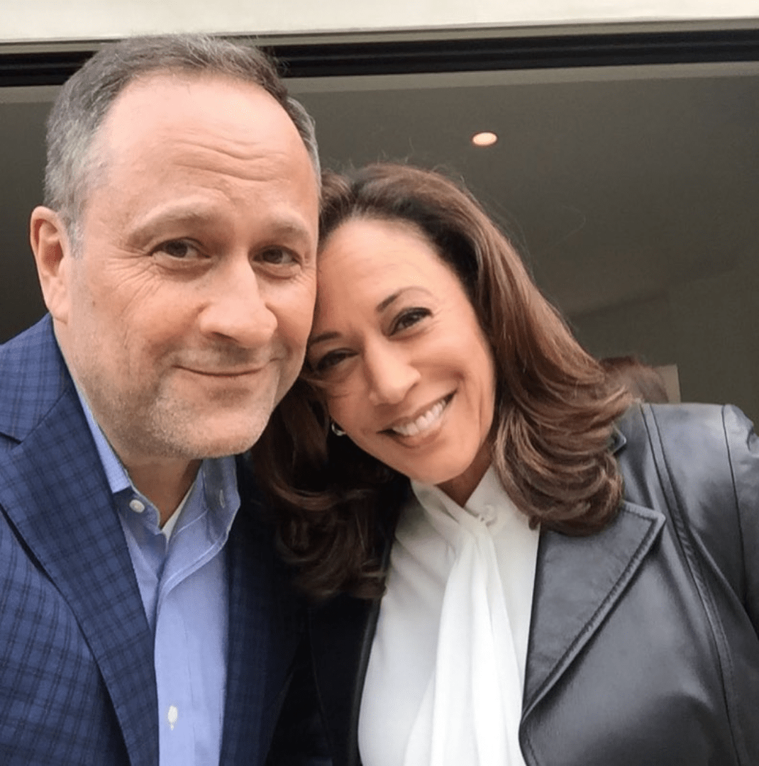 Doug Emhoff is a big, friendly, slightly goofy-looking fellow in a lawyer's fancy blue blazer (but with open collar). He poses for a selfie with his smiling wife.