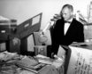 John Glenn dressed in a suit and tie looking at piles of letters