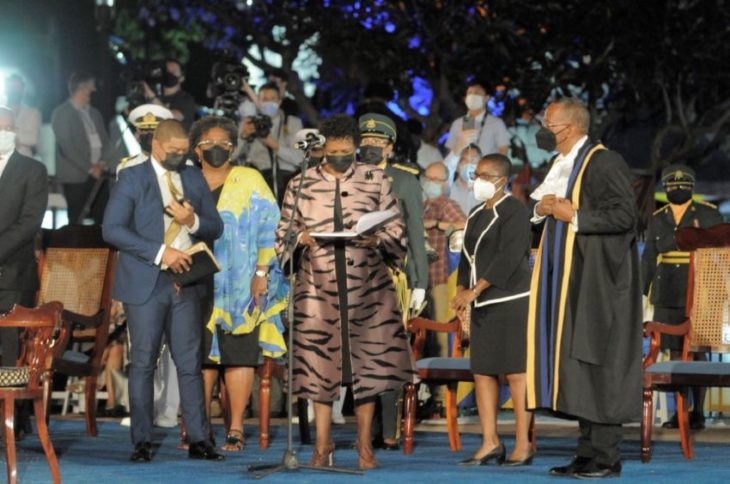A group of formally-dressed people from Barbados stand on a stage (or dais) as an official is installed