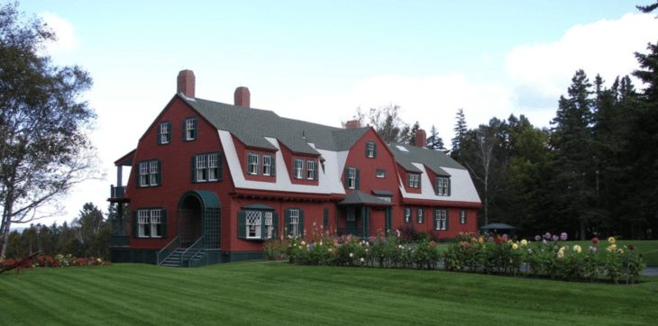 A huge, three-story, barn-like Dutch Colonial mansion set on a bluff overlooking a bay, surrounded by gardens