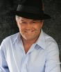 Mickey Dolenz wears a hat and a big smile. He's an older gent but looks good in a cocked Sinatra-style fedora and open-collar shirt