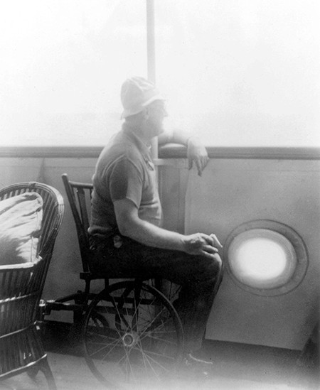 An older-looking FDR sits in a wooden wheelchair at the rail of a large boat or yacht