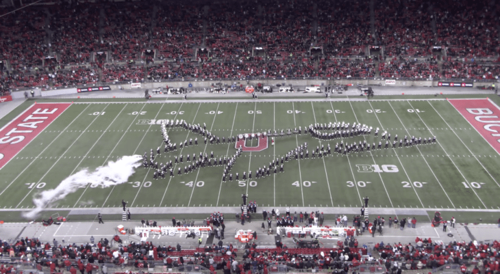 A marching band forms the shape of a fighter jet on a football field