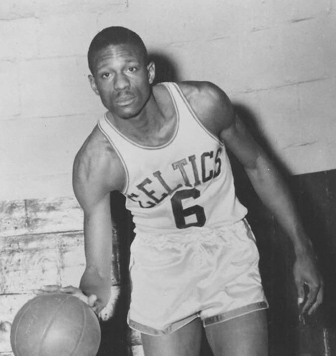 A tall man in a Celtic uniform dribbles a basketball