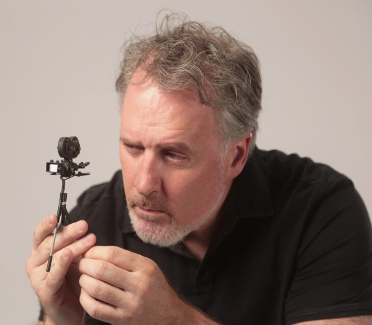 A bearded man peers at a tiny motion picture camera