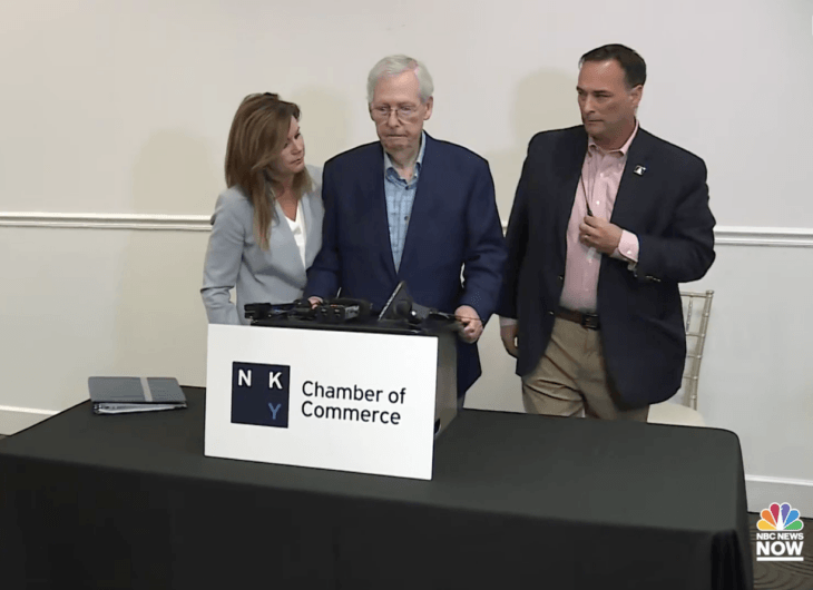 Aides rush to help an old man at a podium